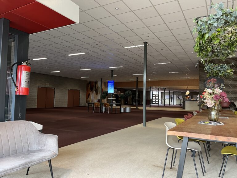 De Centrale Hal gefotografeerd vanuit een zitje bij de hoofdingang, met zicht op de balie, het informatiescherm, een koffiepunt en de ingangen naar het Auditorium